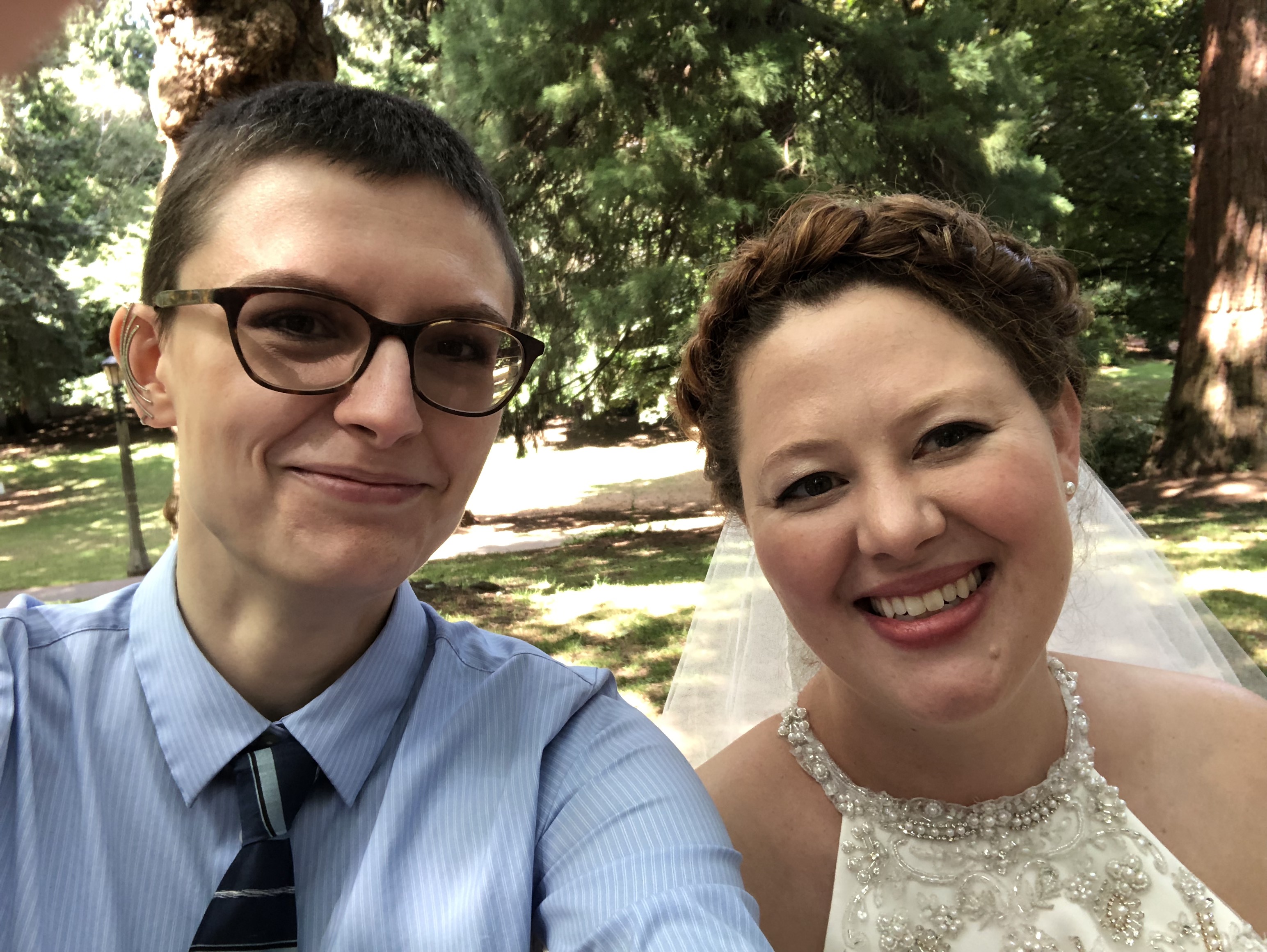 Selfie of me and my friend at her wedding. I'm wearing a blue button up shirt and tie and she's in a white bridal gown with her hair up. We are smiling.